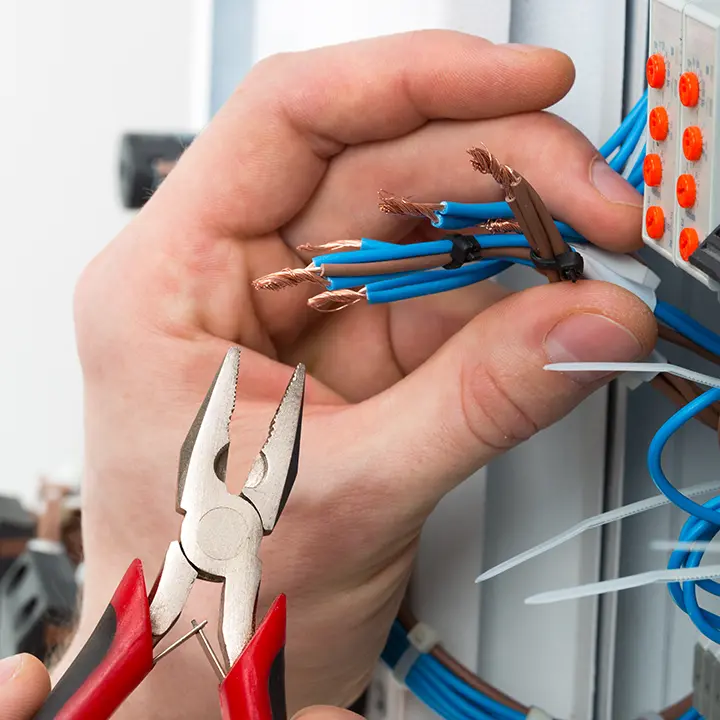 Elektryk naprawiający przewody w instalacji elektrycznej – precyzyjna praca z użyciem narzędzi.